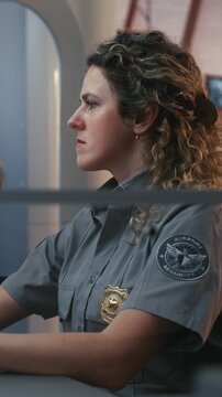 Professional Adult Woman in Airport Security Uniform Works at Surveillance Station, Ensuring Passenger Safety. Reliable Transport Security, Border Protection, and Professional Duty. Vertical Shot.