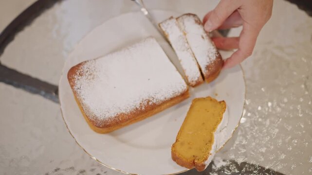 Closeup hands slicing pumpkin loaf dusted with powdered sugar on white plate at glass table, warm morning light, home baker serving golden spice bread with soft crumb, intimate cozy breakfast scene