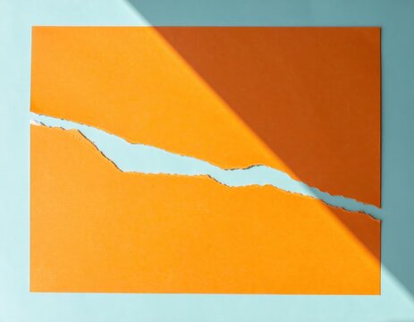 Abstraktes Konzept mit einem gerissenen orangefarbenen Blatt Papier auf hellblauem Hintergrund und einem markanten diagonalen Schattenwurf.