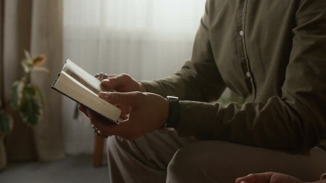 Cinematic tilt up shot of young Muslim couple reading Quran together at home with focus on smiling young man discussing verses with wife, copy space