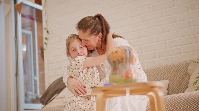 White mother daughter hugging on couch, pumpkin pie on table, soft sunlight through window, mother kissing daughters cheek, warm livingroom atmosphere with cozy textiles and ceramic cup, tender family