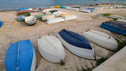 Colorful rowboats and dinghies resting upside down on rocky waterfront under soft daylight, creating quiet seaside harbor mood