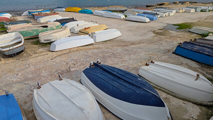 Small dinghies and rowboats arranged upside down on rocky waterfront near calm water, showing quiet coastal storage scene