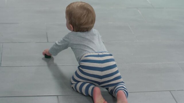 Infant navigates residence. Young child crawling over tiles. Baby carefully advances across tiled ground inside home. Small child explores and moves across shiny tiled flooring in quiet house