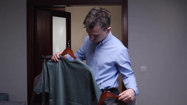 Young man choosing a t shirt from a portable clothing rack at home, deciding a smart casual outfit for the day in a neutral, modern wardrobe setting