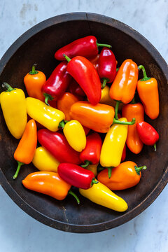 Red, yellow and orange mini sweet peppers in a black wood bowl 