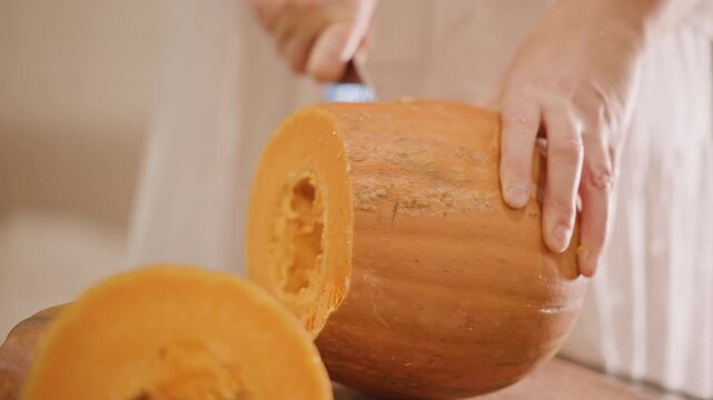 Close up person carving pumpkin with knife, steady hands slice thick rind into even segments on wooden board, seeds removed and inner flesh exposed, careful kitchen prep for pumpkin pie filling,