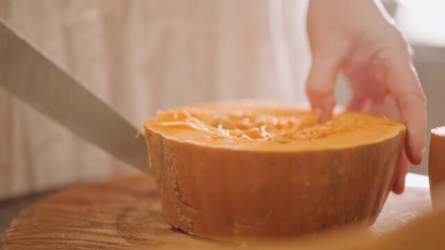 Pumpkin halves ready for slicing, closeup of hands scoring orange flesh with large knife on wooden board, careful scooping of seeds and strands, warm studio light, stepbystep prep for pumpkin pie