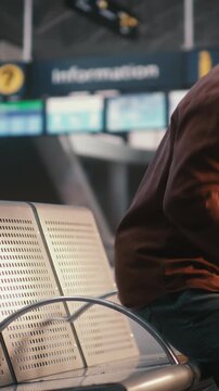 Black Male, Pulling Suitcase Enters Airport Waiting Area. Man Uses Smartphone Scan Boarding Pass, Glances Between Device and Overhead Flight Information Boards Confirm at Correct Gate. Vertical Shot.