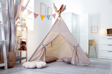 Stylish toy wigwam, furniture, pillows and decor in light playroom. Interior design © New Africa