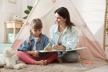 Mother and her daughter drawing in sketchbook together near toy wigwam at home © New Africa