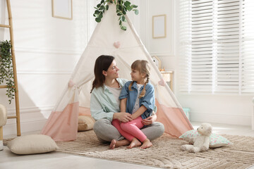 Mother and her daughter near toy wigwam at home © New Africa