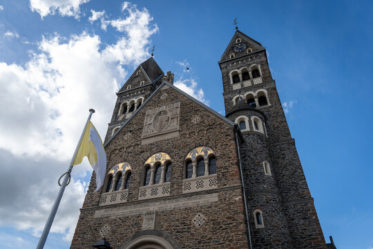 Clervaux church front facade with twin towers and Vatican flag against blue sky