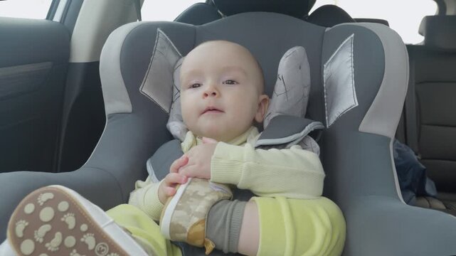caucasian baby smiling in car seat with feet up shoes. Playful giggles and bright expression, daylight through window, secure harness. concept of child safety in a child seat