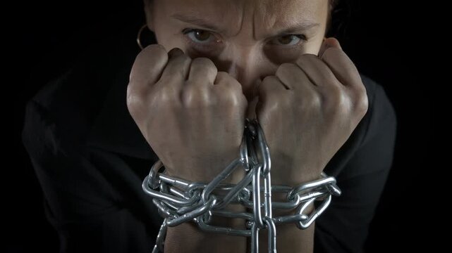 Female hostage in chain. View of female hostage sitting in the dark with chained hands against black background