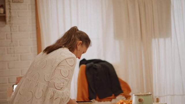 White woman reading with pumpkin pie by window, sitting at small round table draped in orange throw, jacket on chair, warm lamp glow, slice on plate, mug steaming, reflective posture, quiet afternoon