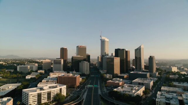 Pulling back camera rising over freeway revealing city skyline at golden-hour, with cloverleafs