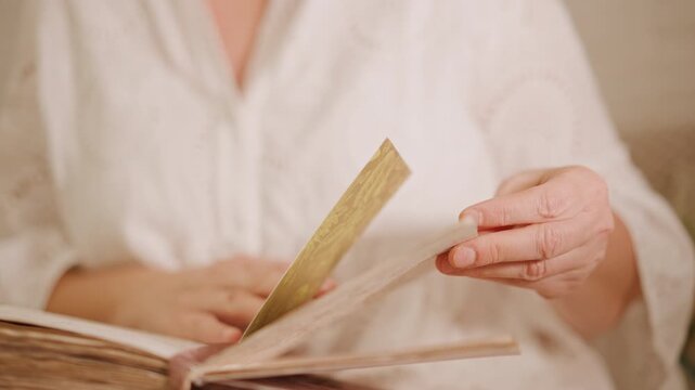 Hands flipping recipe book white woman turning pages sliding ribbon bookmark revealing handwritten notes closeup of leatherbound cover gentle wrinkled hands warm soft light cozy autumn baking vibe