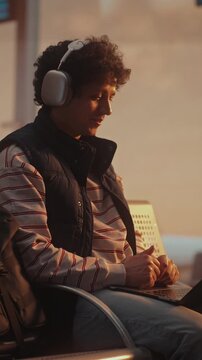 Professional Having Business Video Call at Airport with Plane Departing Behind. Man With Curly Hair Engages in Important Business Meeting Via Laptop. Concept of Global Communication. Vertical Shot.