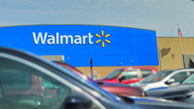 Exterior view of a Walmart store facade with the blue branding and spark logo with blurred cars in the foreground (Minnesota, USA - March 29, 2026). Editorial Use Only.
