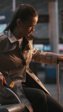 Female Traveler Comparing Digital Ticket With Airport Information Board. Woman Looks Up Overhead Flight Board, Cross Referencing Gate Number, Departure Time With Data on Screen. Vertical Shot.