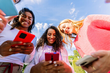 Obraz premium Close up of women using smartphones together outdoors. Diverse female friends connected through mobile technology and social media. Digital connection and online lifestyle concept.