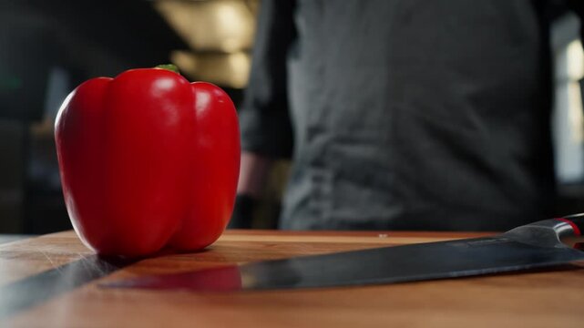 A chef in the kitchen prepares to chop a red pepper, his hands in gloves in the frame.