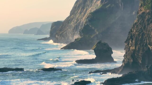 Waves crash against the rugged cliffs and sea stacks of Karekare Beach, New Zealand. The wild, untamed beauty of the coastline is a popular destination for surfers.