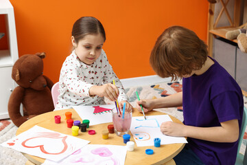 Obraz premium Cute little friends drawing together with brushes and paints at table indoors