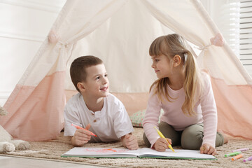 Little kids drawing in sketchbook together near toy wigwam at home © New Africa