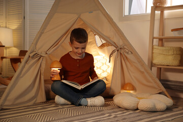 Little boy reading book in toy wigwam at home © New Africa