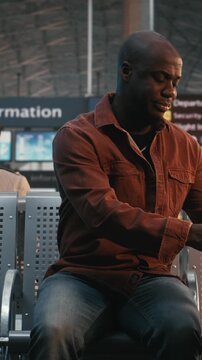 Man Arrives at Airport Waiting Area, Sets Down Luggage, Immediately Checks Smartphone. Modern Habit Staying Connected, Checking Flight Updates, Chatting With Friends Before Departure. Vertical Shot.