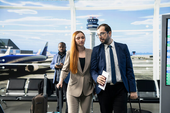 CEO and executive assistant approaching boarding gate in airport lounge, preparing for international flight. Two business travelers with baggage and boarding passes ready, leadership collaboration.