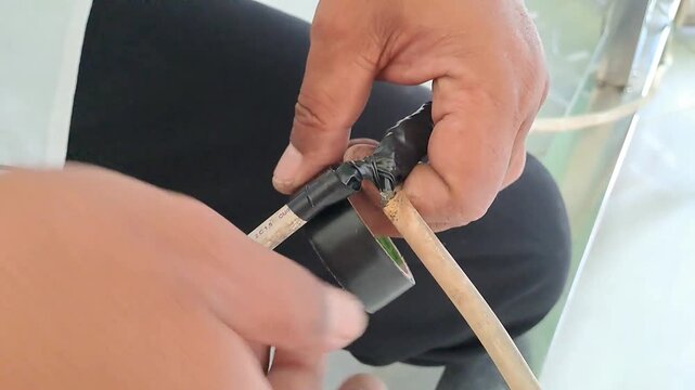 PAMEKASAN, INDONESIA - DECEMBER 15, 2025: Handheld footage of an Asian man repairing exposed electrical cables, insulating wires to prevent short circuits, electric leakage, and electrocution, high.