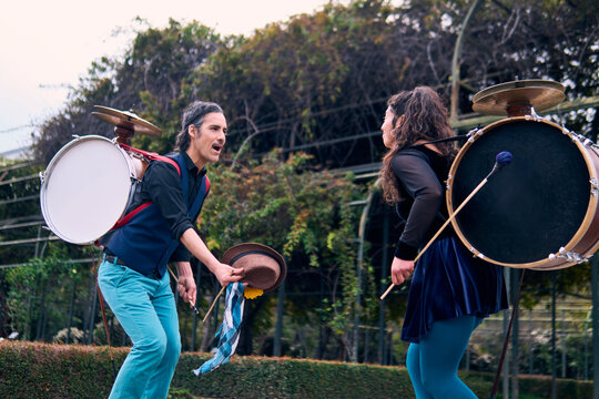 Adult couple of urban dancers, happily playing and dancing the cueca with a bass drum on their backs outdoors, Chilean chinchineros, street musicians who play the bass drum and dance in the streets.