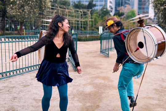 A pair of urban dancers, playing, dancing romantically, and joyfully the cueca with a bass drum on their backs outdoors, Chilean chinchineros, street musicians who play the bass drum and dance.