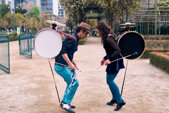 A pair of urban dancers, playing, dancing romantically, and joyfully the cueca with a bass drum on their backs outdoors, Chilean chinchineros, street musicians who play the bass drum and dance.