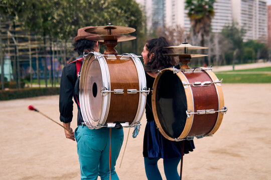 A pair of urban dancers, playing, dancing romantically, and joyfully the cueca with a bass drum on their backs outdoors, Chilean chinchineros, street musicians who play the bass drum and dance.