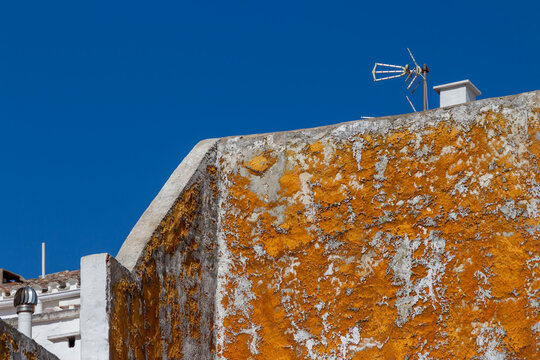 Old wall with peeling orange paint and rooftop against blue sky in Menorca