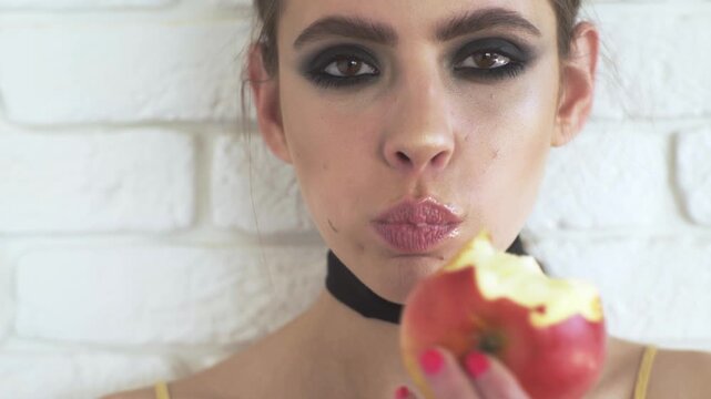 Sensual woman bite apple with makeup and sexy lips. Girl portrait closeup eating juicy apple with smoky eyes. Young woman eating apple with natural beauty. Female face with fresh apple.