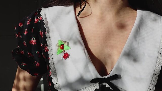 A beautiful little handmade martisor with a ladybug and flowers, pinned to the left side of a young woman's white vintage dark dress collar, seen on a sunny day, close-up from the side with slow motio