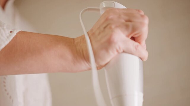 Caucasian hand gripping immersion blender motor, firm wrist control with cord wrapped over forearm, steady downward motion and focused technique, handson kitchen skill finishing pie filling.
