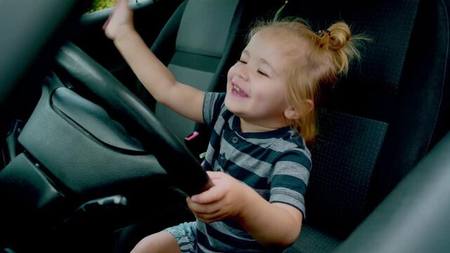 Child driver holding wheel inside vehicle interior. Toddler driving car. Baby driver touching steering wheel with curious expression. Kid sitting in seat playful imitation driving.