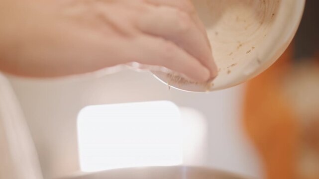 Sprinkling spice over pumpkin batter closeup, pinch of cinnamon and nutmeg dusting mixture, steam rising, soft backlight highlighting ceramic bowl rim, finishing touch by pastry cook, intimate