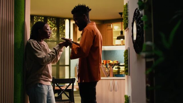 Black boyfriend seeing her girlfriend laugh at mobile phone screen, being suspicious about a potential affair, worrying about infidelity and dishonesty. Controlling toxic man in rage, bullying.