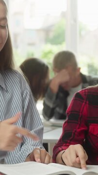 Happy joyful Caucasian teen girls talking discussing book with classmate lesson in classroom school education learning schoolgirls teenagers friendship study cooperation students reading literature