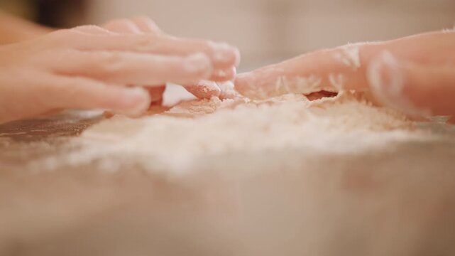 White hands kneading flour on table, closeup of fingers and palms pressing and folding dough for pumpkin pie crust, mentor and child exchanging technique, tactile rhythm, warm countertop, recipe