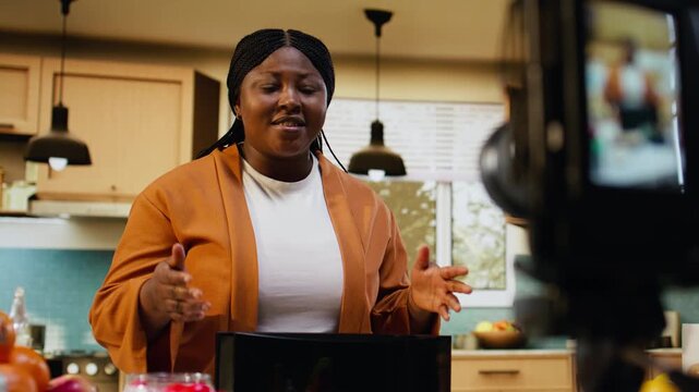 Black content creator presenting avocado on toast recipe and filming, recording a healthy food choice in kitchen studio. Using a toaster on the counter and presenting meal prep on camera.