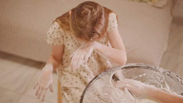 Joyful baking chaos. Happy child plays with flour during kitchen baking adventure at home. Smiling girl experiences delightful baking chaos with flour during pumpkin pie preparation at home