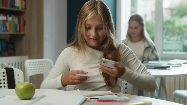 Focused Caucasian little girl child using mobile phone writing test in classroom cheating AI assistant kid schoolgirl student dishonest study pupil teenager exam task internet education problem school